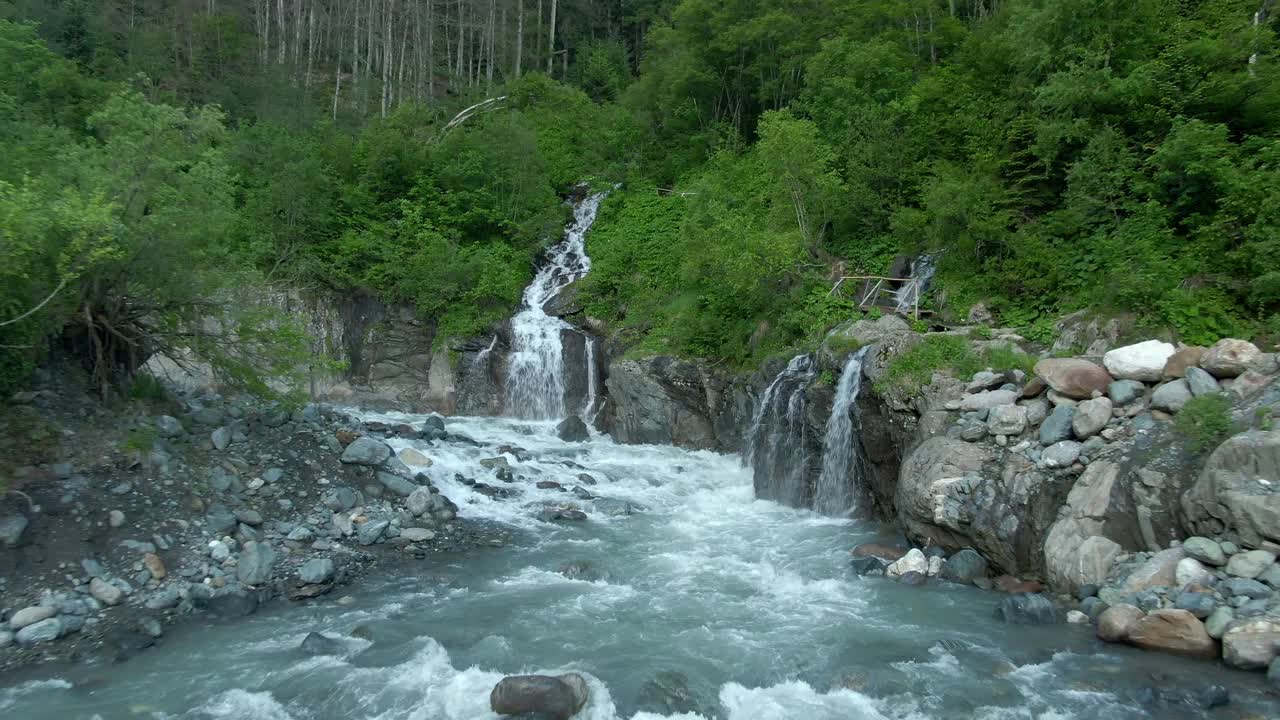 鸟瞰图飞越湍急的山河与风暴瀑布。美丽的山景，河流和瀑布的背景是绿色的森林。登山之旅视频下载