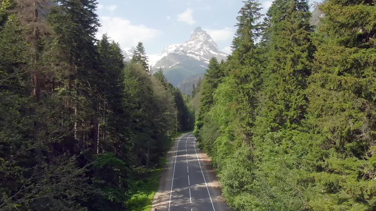 鸟瞰图飞行在一个美丽的山路与开放的美丽全景的山峰覆盖积雪的背景绿色的森林。开车到山里去。一家人在山里度假视频素材