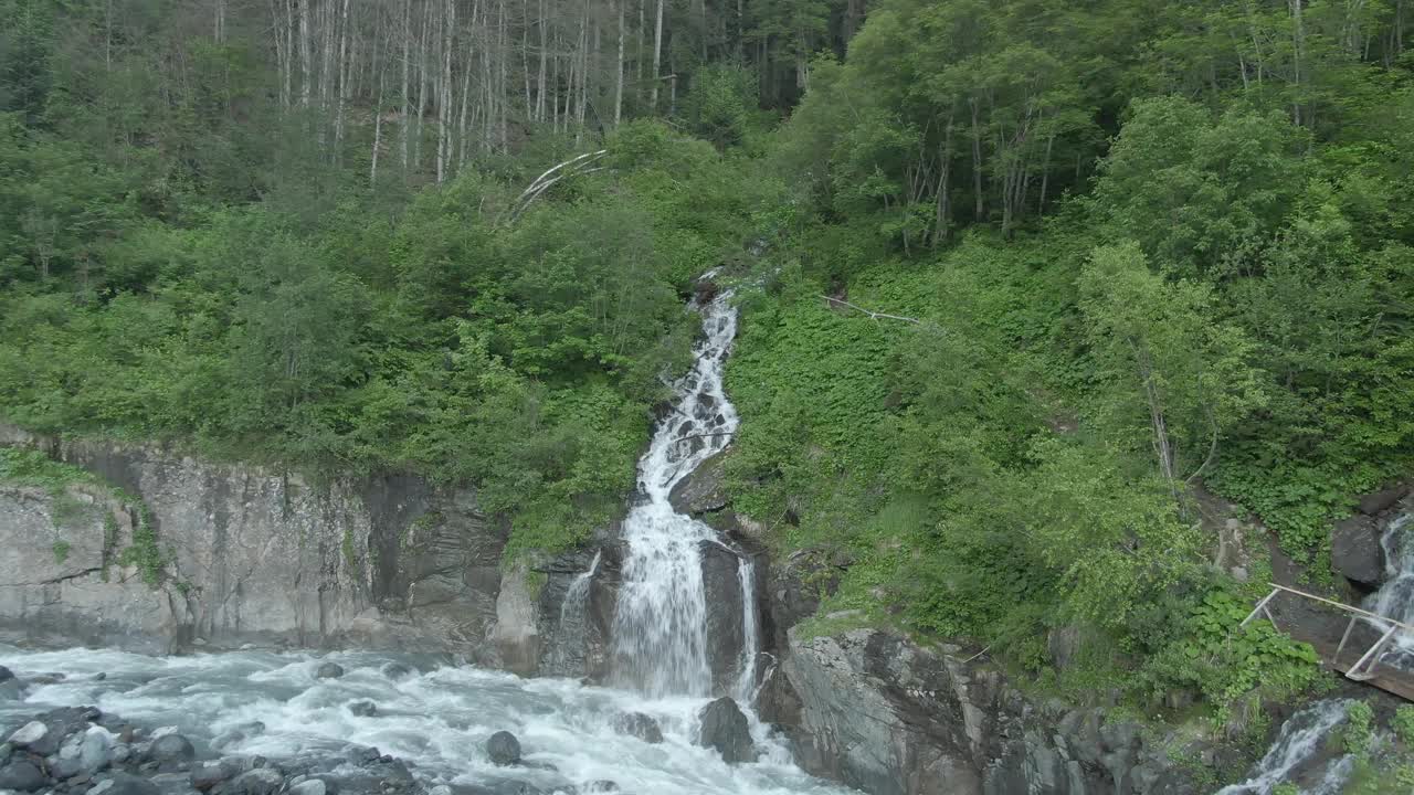 鸟瞰图飞越湍急的山河与风暴瀑布。美丽的山景，河流和瀑布的背景是绿色的森林。登山之旅视频素材