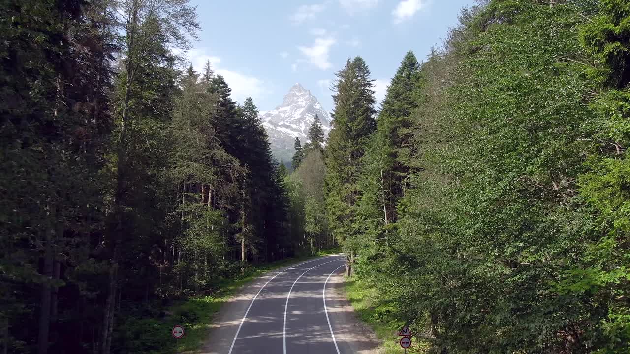 鸟瞰图飞行在一个美丽的山路与开放的美丽全景的山峰覆盖积雪的背景绿色的森林。开车到山里去。一家人在山里度假视频下载