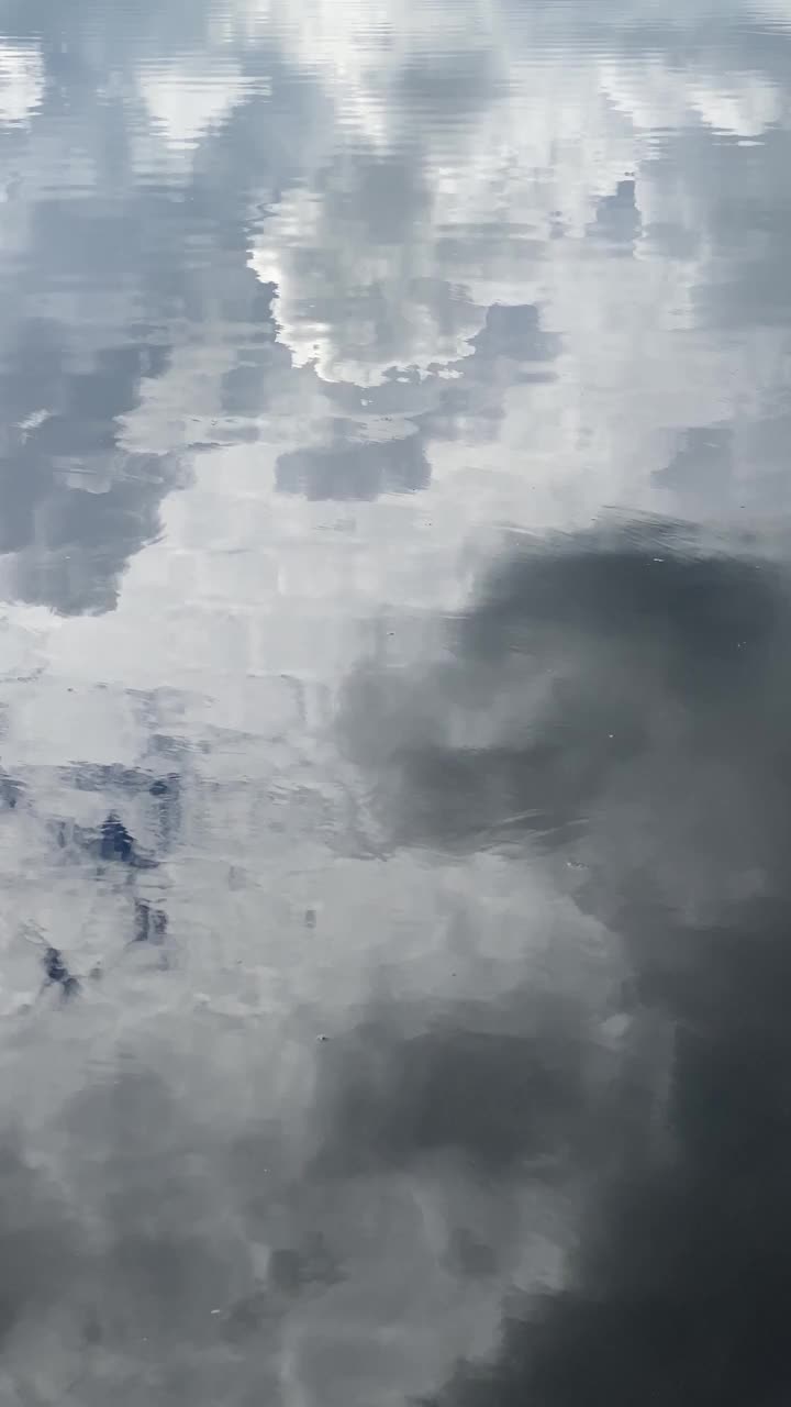 在雷雨前-多云的天空在湖面上反射出白色和灰色的色调，水面上有光波和气泡。视频下载