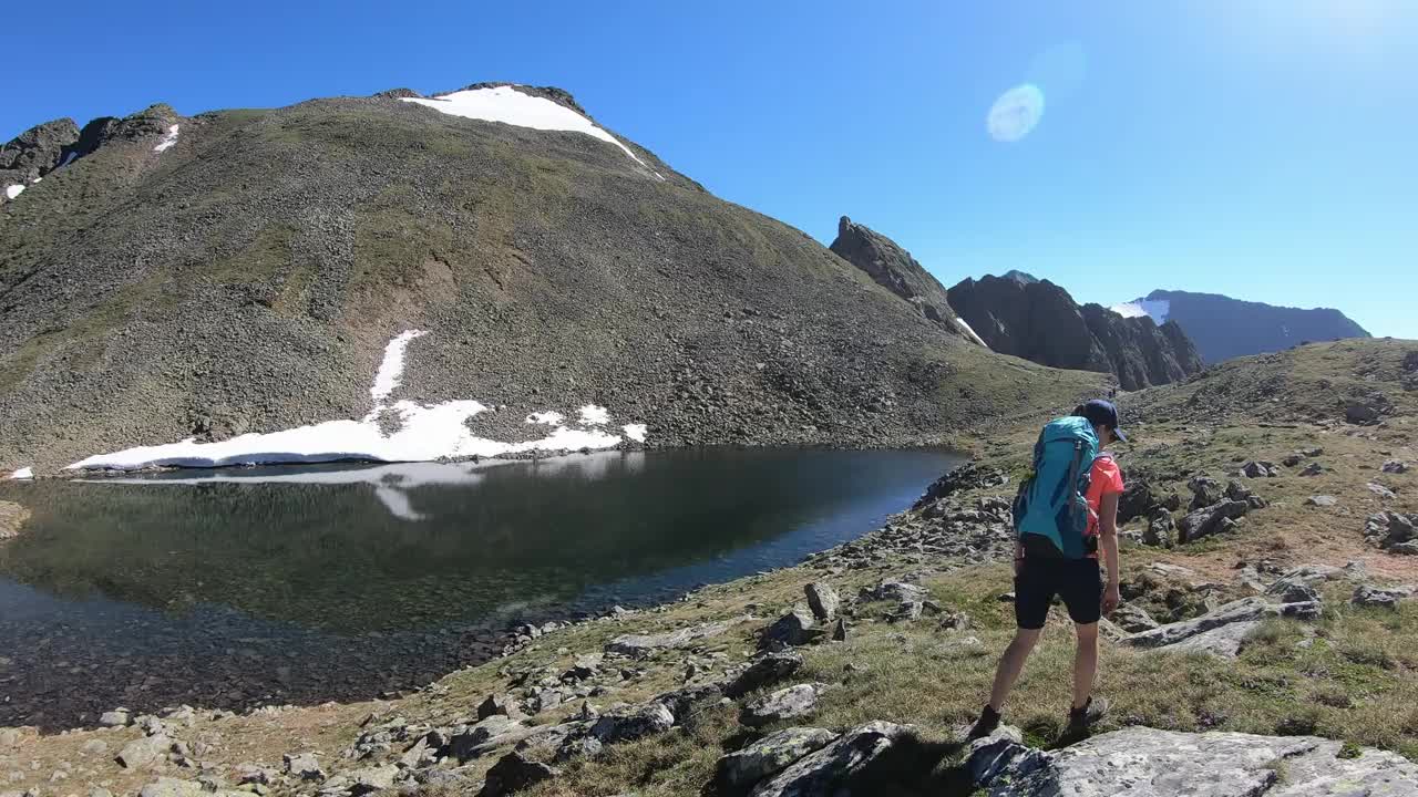 一个背着大背包在Schladming附近的奥地利阿尔卑斯山徒步旅行的女人。她沿着高山环抱的小湖走着。山坡上有些雪。在野外露营。阳光明媚的一天。视频素材