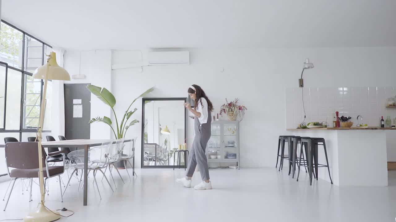 一般看迷人的年轻女子在宽敞的公寓里跳舞，在家里听着喜欢的音乐。微笑的女士在客厅里玩耍，跳跃和旋转，感觉快乐，慢动作。视频素材