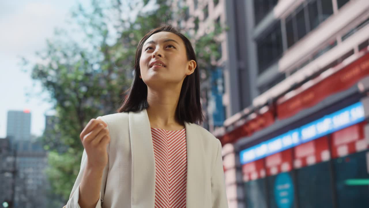 美丽的日本女性的肖像穿着漂亮的休闲衣服在街上摆姿势。在大城市生活的成功女性。背景与办公楼和广告牌。视频购买