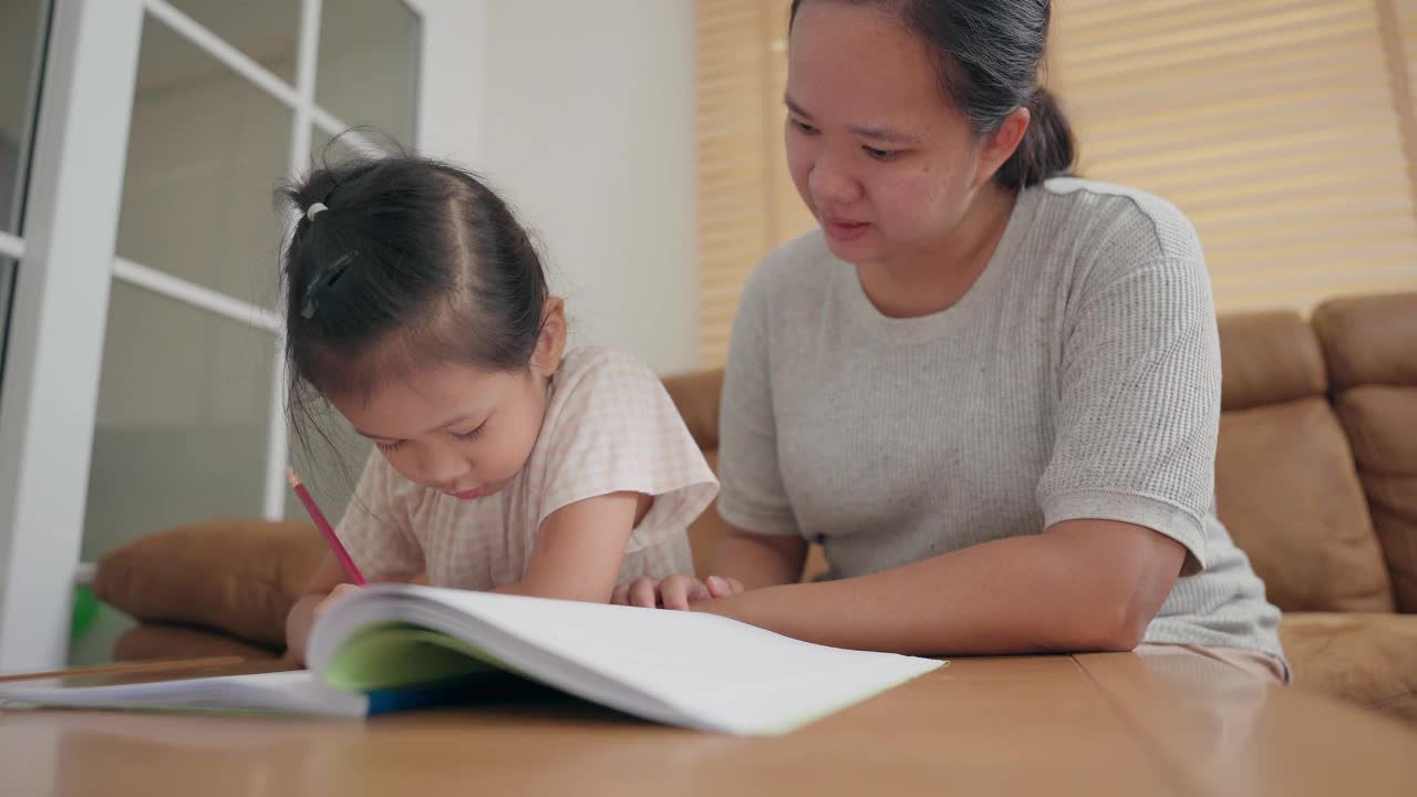 亚洲母亲照顾她的小女孩学习写在学校作业在家里视频素材