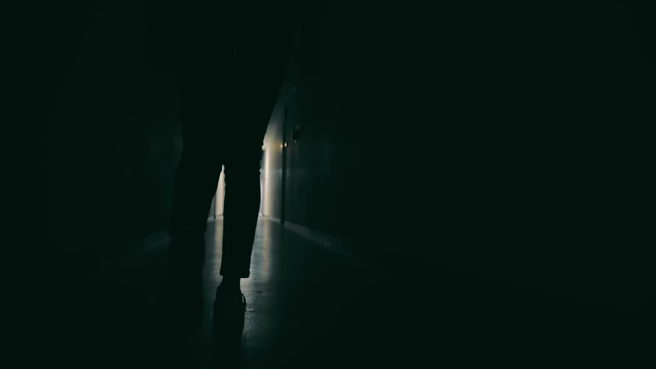 黑暗的走廊上女性的腿的剪影。一个女人去了走廊尽头的一个灯火通明的会议视频素材