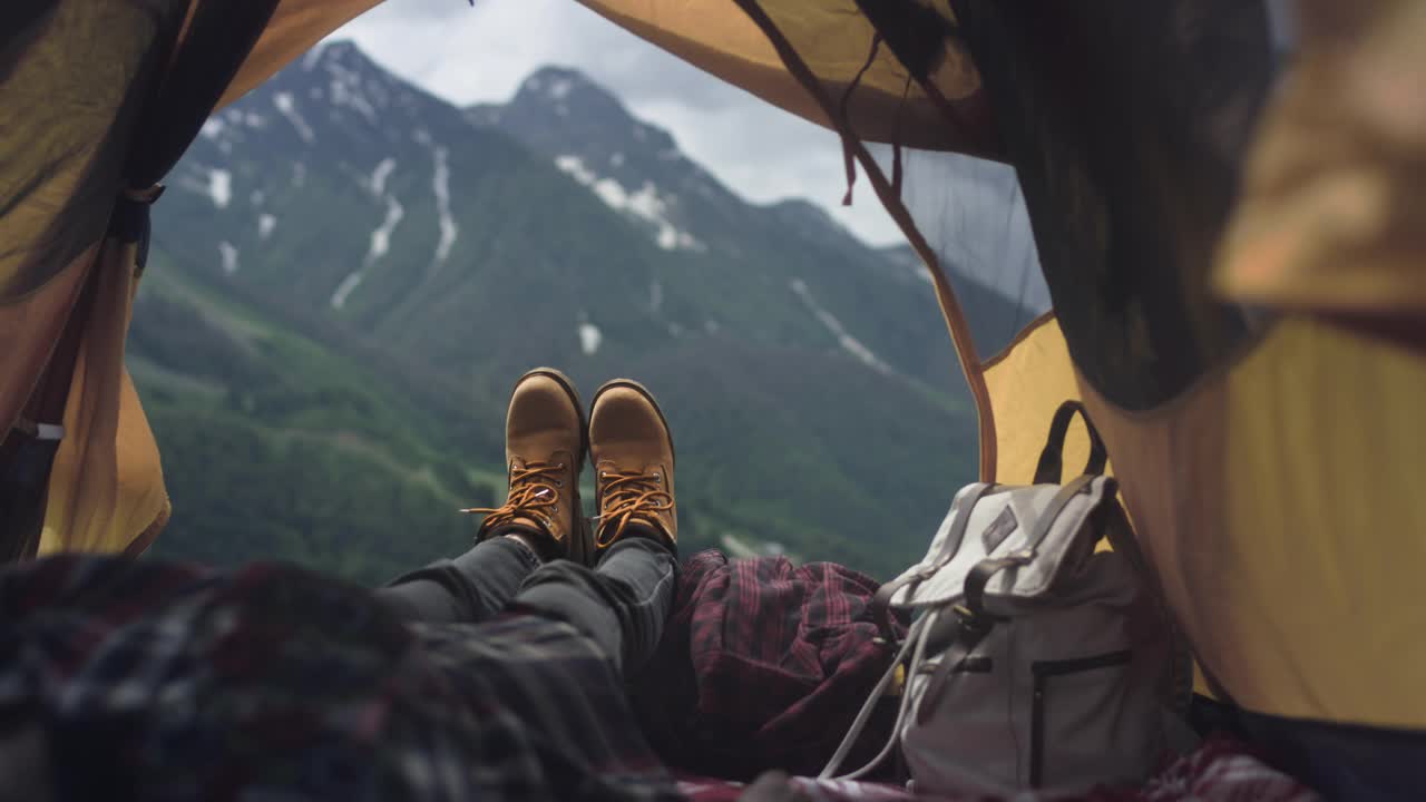 穿着黄色登山靴的女人的腿躺在黄色帐篷里。旅行者正在休息，欣赏着爬过的山视频素材