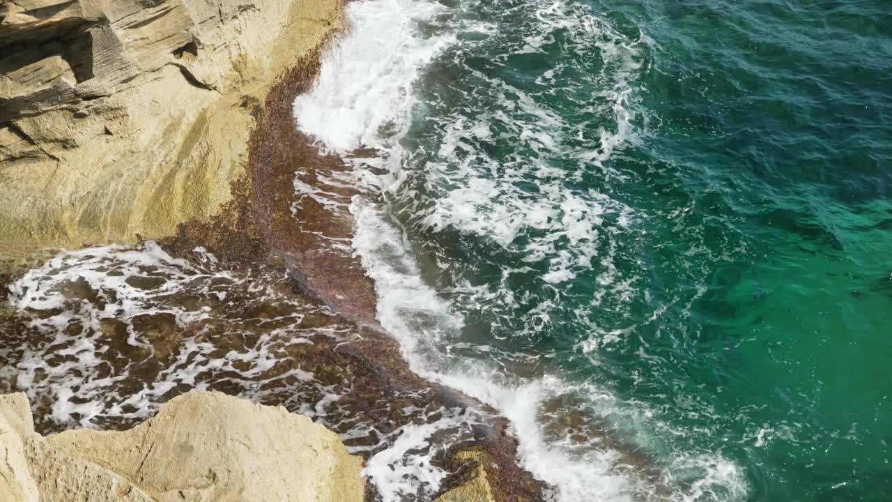 在一个阳光明媚的日子，从上面看，小海浪拍打着岩石海岸视频素材