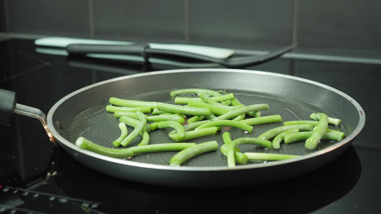 男人的手把青豆放在煎锅里。专业厨师用豆子做菜。在锅里煮绿豆荚视频素材