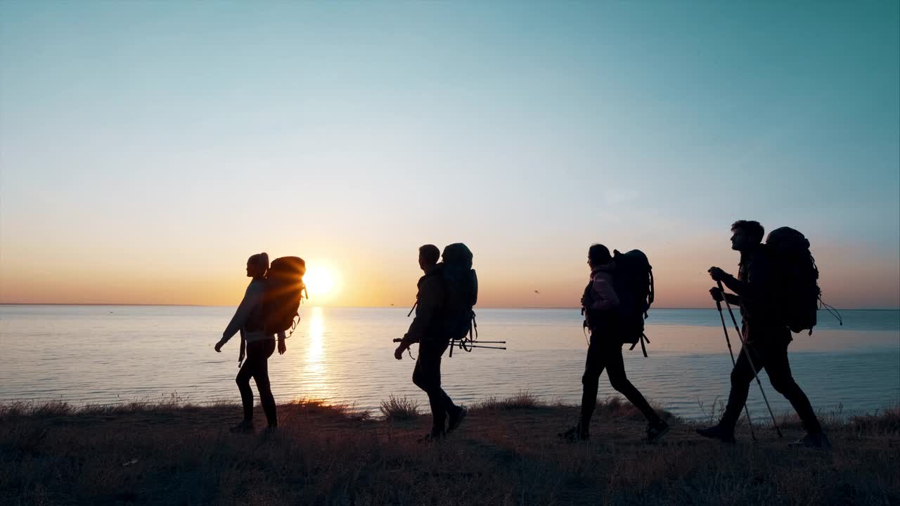 四个背着背包的旅行者在海边散步。慢动作视频素材