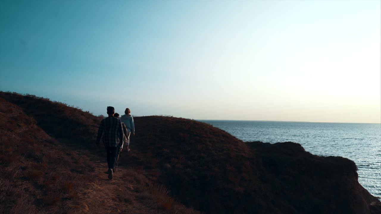 三个人背对着海景走在山上视频素材