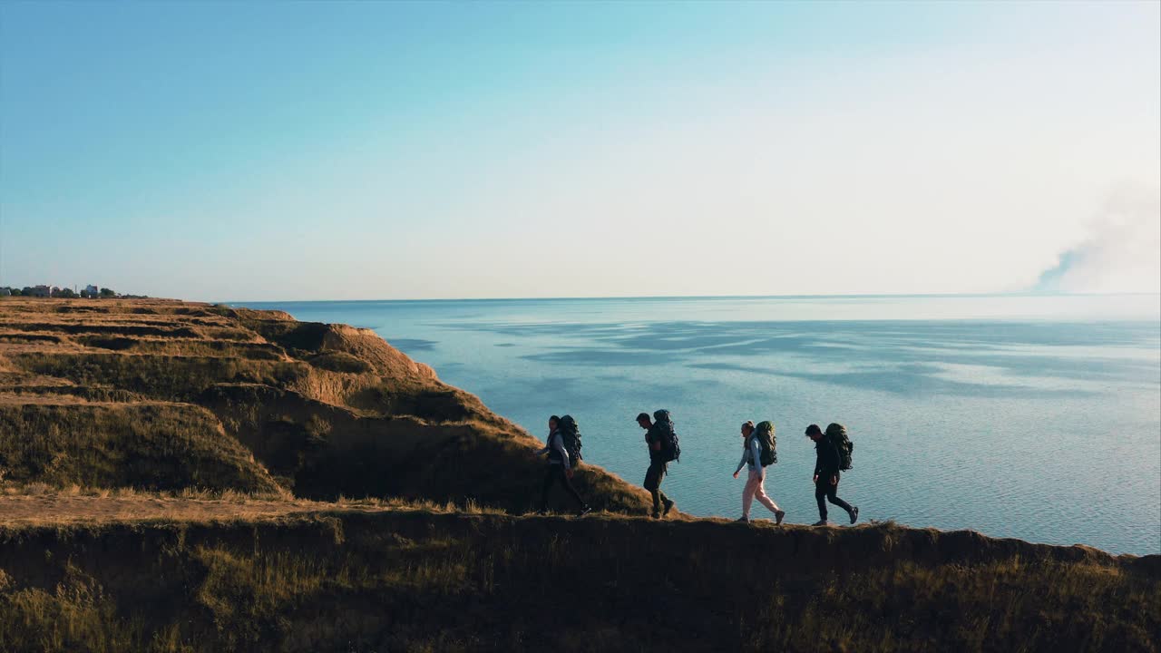 四个人背着背包，背对着海景走在山间视频素材