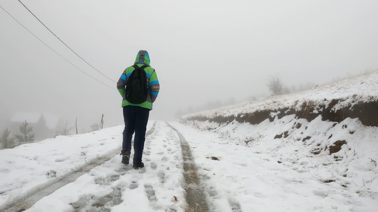 一个男人背着双肩包在山上的雪地上行走的冬季场景视频素材