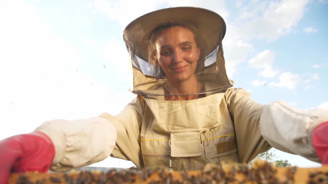 一个穿着防护服的女养蜂人拿着一个装着蜂巢蜂蜜的架子视频素材