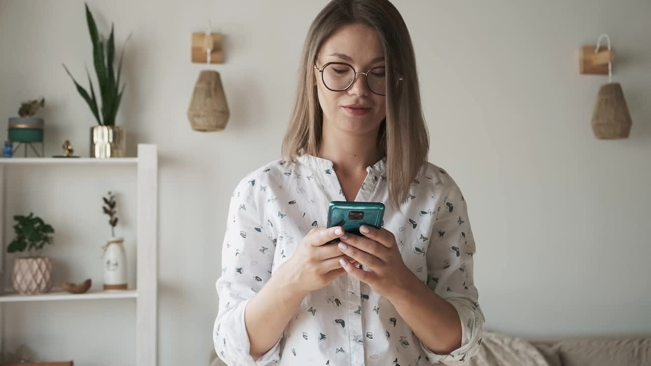 戴眼镜的女人用手机发短信，在家微笑视频素材