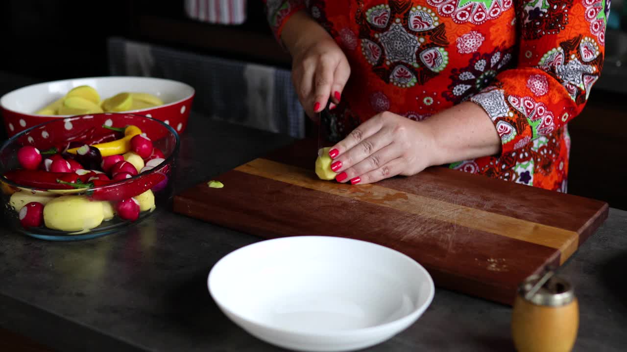 在她的现代厨房里，一位中年妇女正在切生土豆，准备她最喜欢的素食视频素材