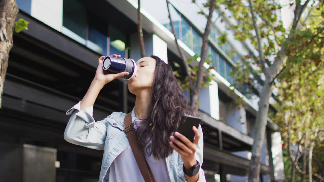 一个亚洲女人一边用智能手机走路一边喝外卖咖啡视频素材