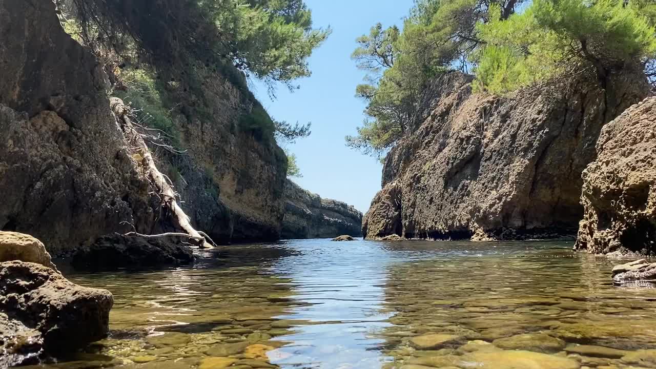 天堂夏天的风景。海峡谷与闪亮的蓝色清澈的水。布满岩石的海滩，有野花、草本植物和茂密的针叶树。孤独的地方。夏季。假期。幸福。地中海沿岸。阳光明媚的一天。视频素材