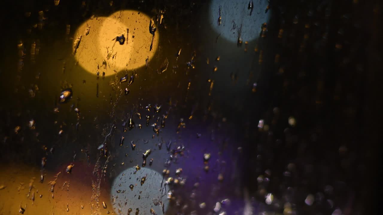 夜雨滴在肮脏的窗户上，背景是散景的灯光视频素材