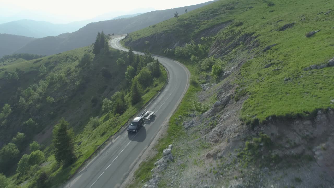 在森林山路上，一架无人机尾随着一辆拖着空拖车的黑色SUV视频素材