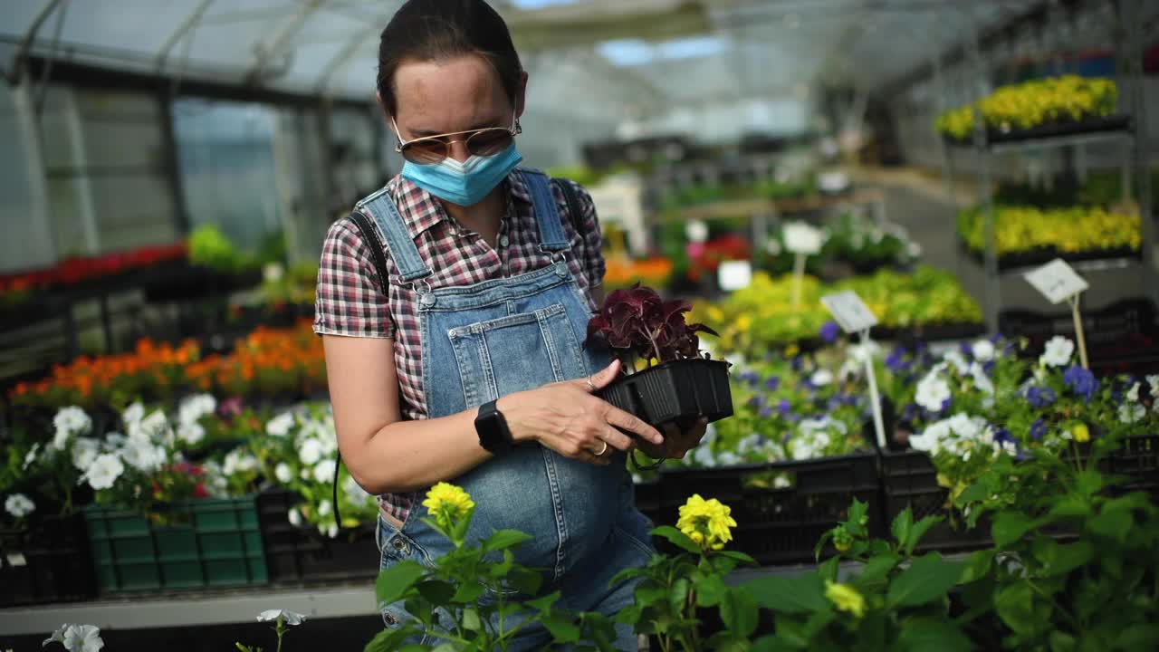 戴着保护面罩的孕妇在花园中心购买植物视频素材