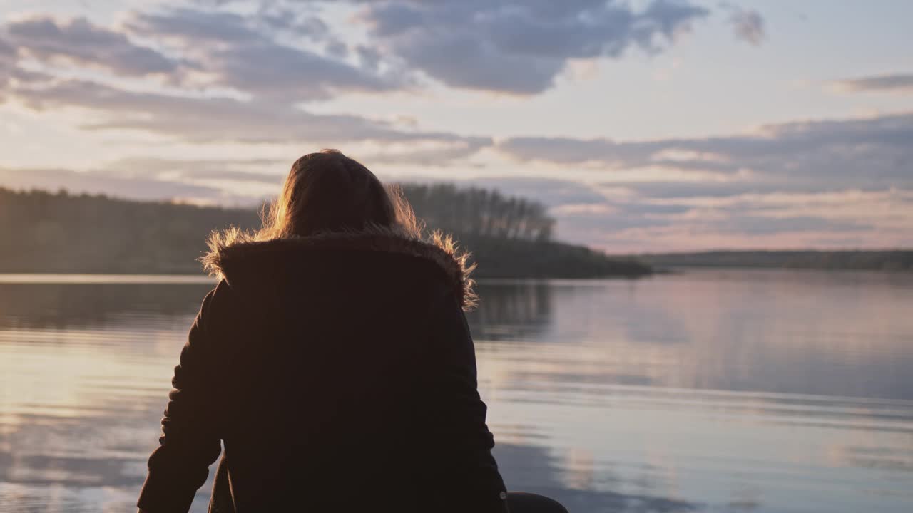 在夕阳的余晖中，一个女人坐在湖边视频下载