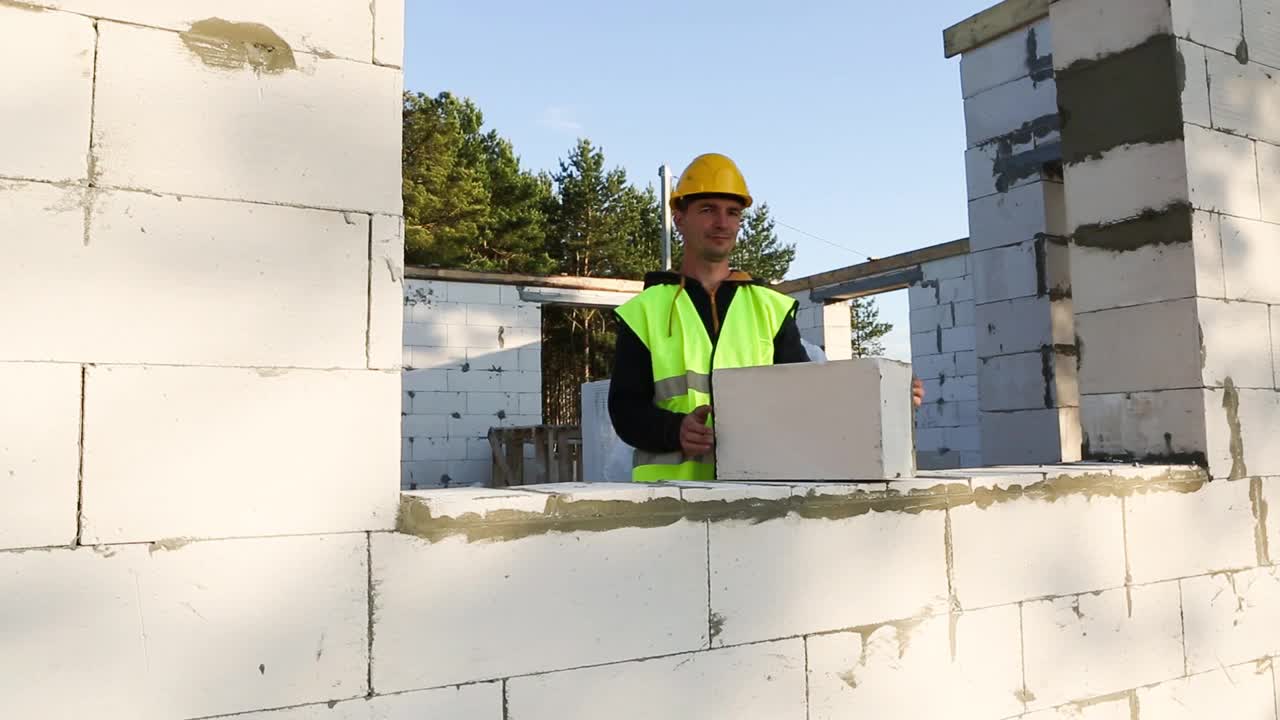 建筑工人在建筑工地上用加气混凝土块砌墙。防护服——安全帽和背心，施工过程中视频素材