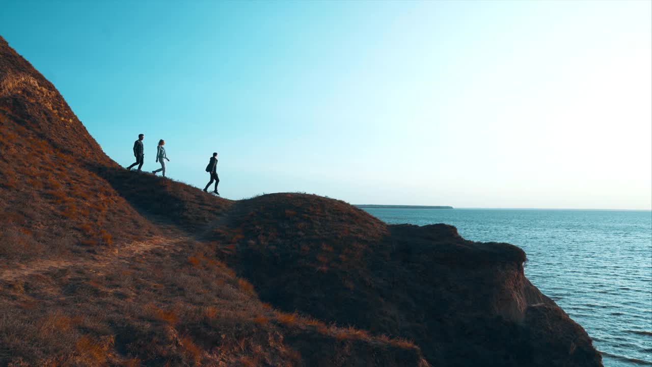 三个人沿着山走到海边视频素材