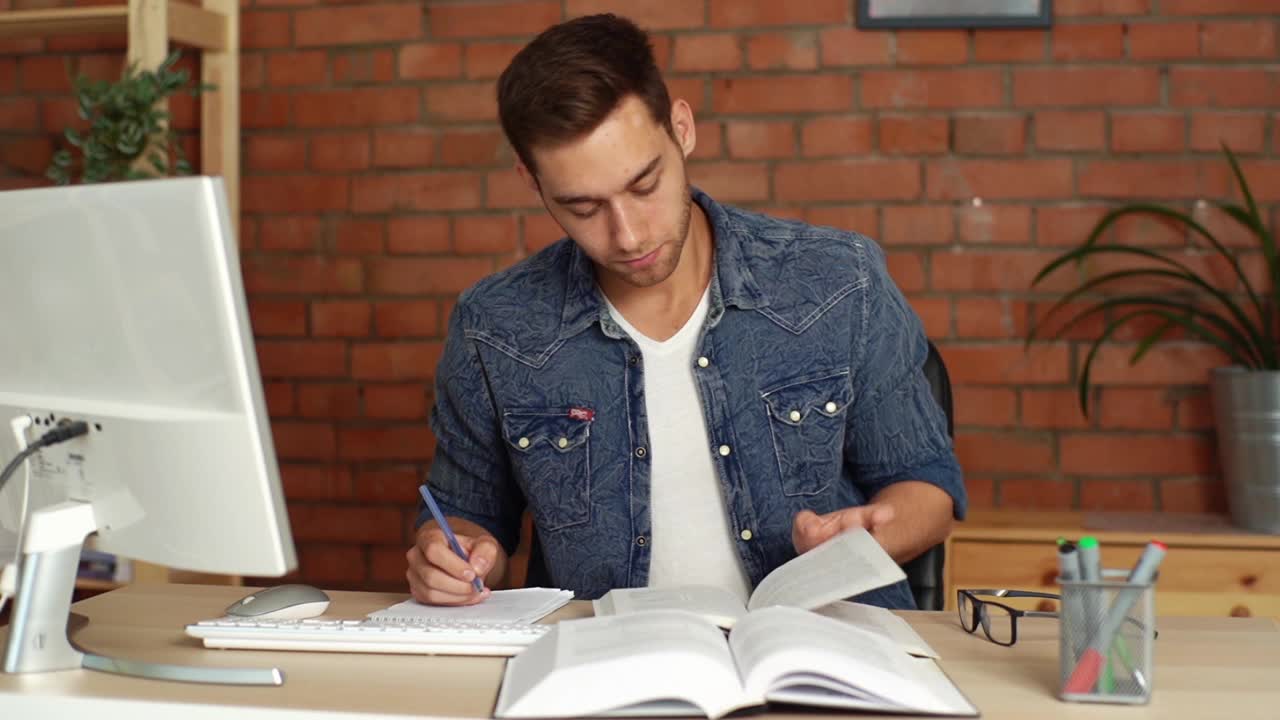 正面视图的焦点年轻男大学生学习，准备考试，写笔记在纸上笔记本与笔。视频素材