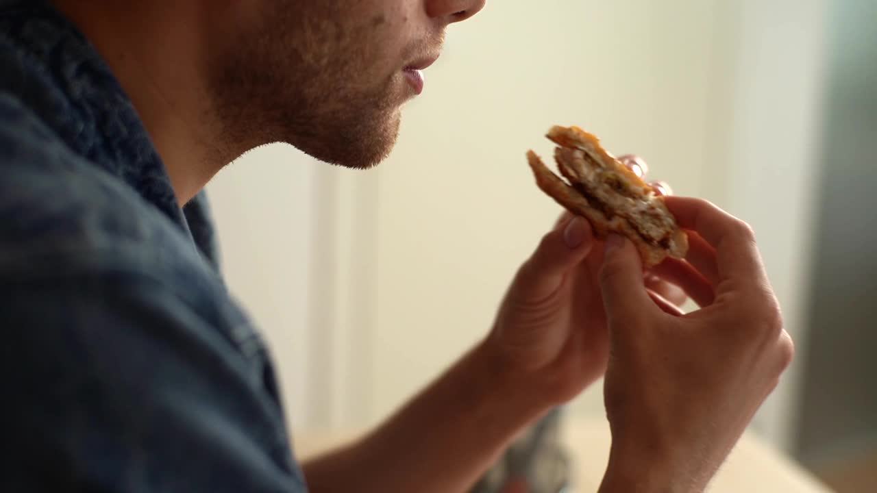 特写脸的年轻人吃汉堡包与牛肉从快餐店和舔手指。慢动作拍摄。视频素材