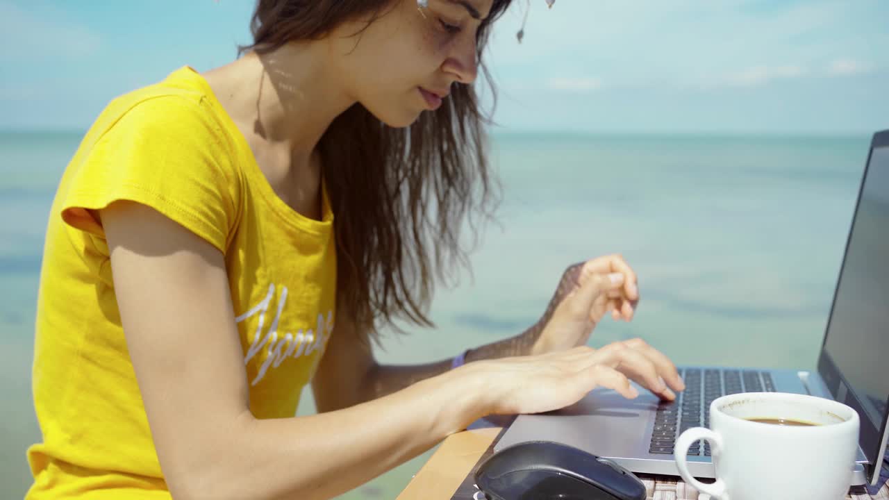 侧视图夏季自由女工作在笔记本电脑在蓝色的海期间，她的旅行视频素材