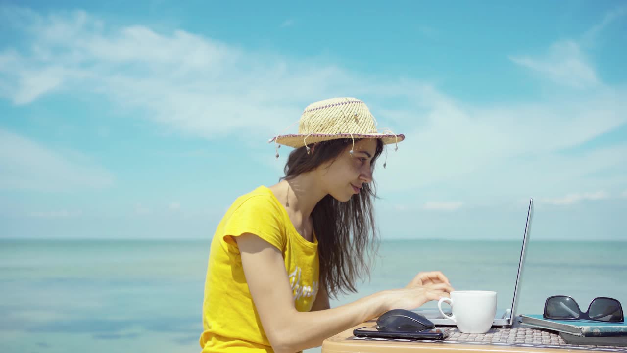 侧视图夏季自由女工作在笔记本电脑在蓝色的海期间，她的旅行视频素材