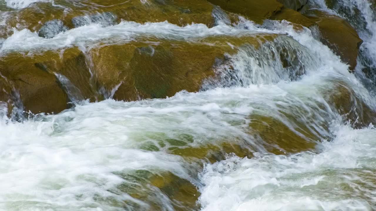 山上的河流，清澈的绿松石般的水在湿的漂砾之间如瀑布般泻下，漂砾上有厚厚的白色泡沫。视频素材