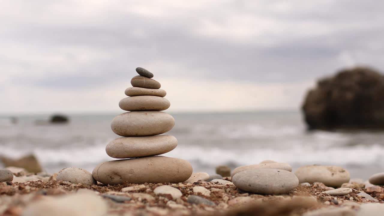 金字塔上的石头在一个阳光明媚的日子里在蓝色的大海背景。女孩的手摧毁了金字塔。节日快乐。卵石滩，平静的大海，旅游目的地。有选择性的重点视频素材