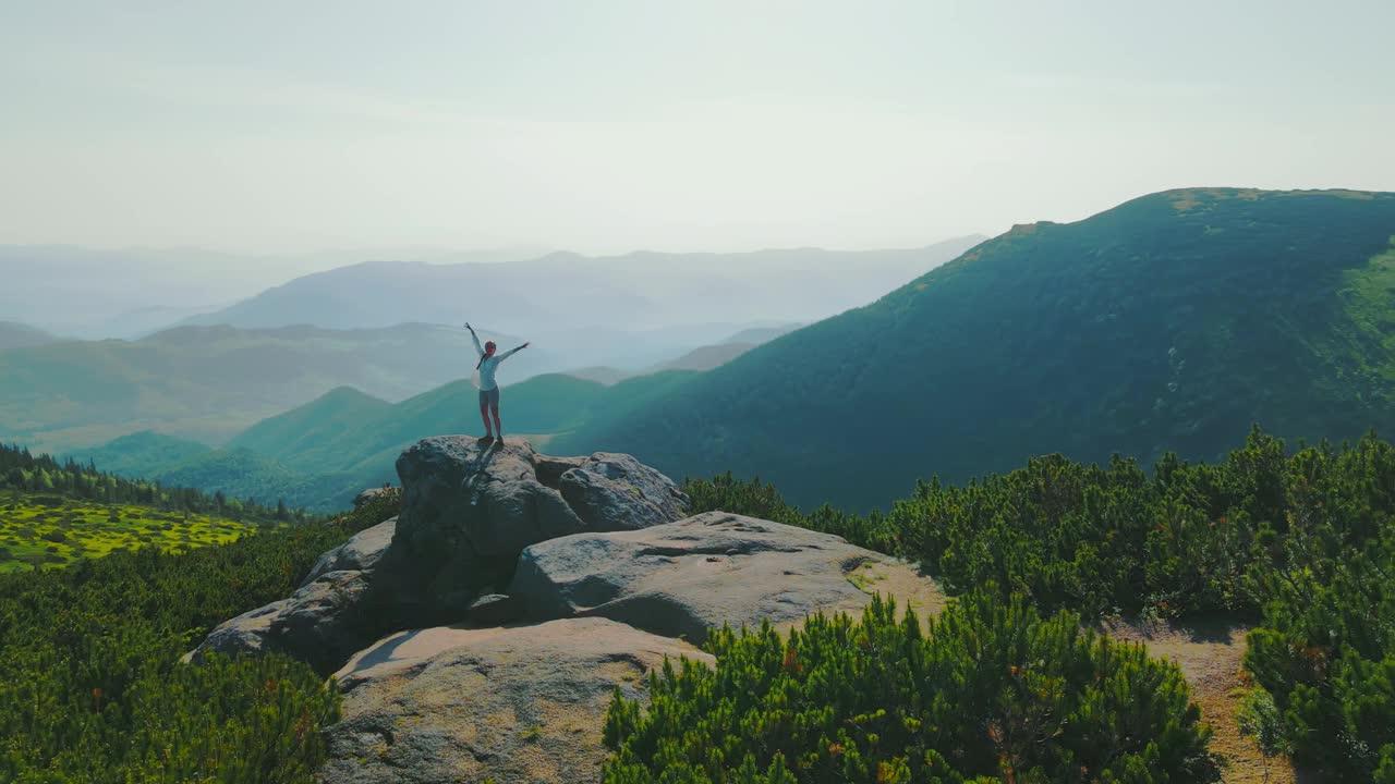 快乐的女人徒步旅行者在山上旋转站在一块岩石上举起手臂。晨曦中的山景在日出时。乌克兰喀尔巴阡山脉的全景视频素材