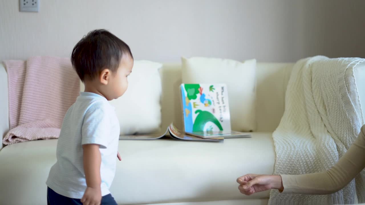 亚洲可爱的男孩学走路的第一步走到他的母亲在家里。小男孩赤脚走在地板上给他的妈妈。视频素材