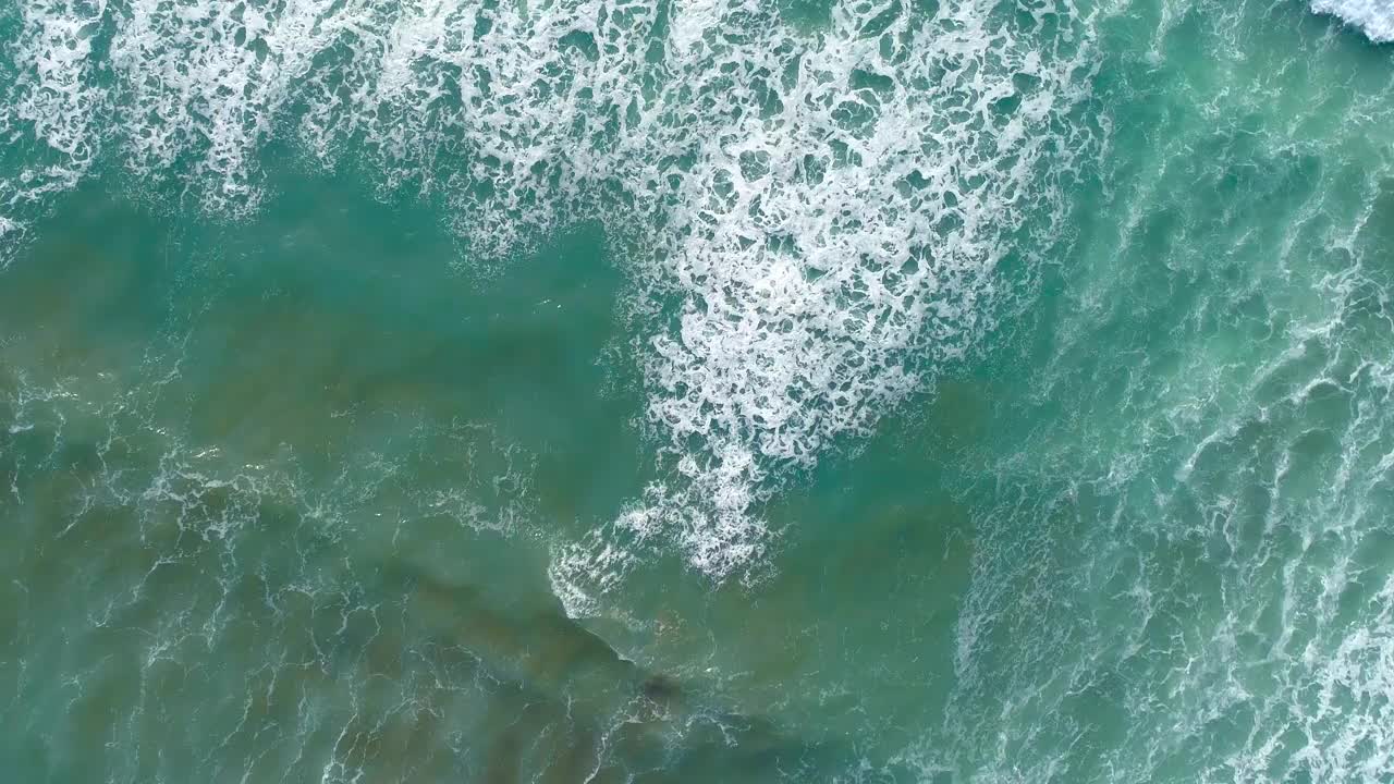 海浪从上面翻滚。从上到下4k无人机观看蓝色的绿松石海洋，破浪，白色。海面上晴朗的一天。巨大的海浪冲击着海岸线。强大的波视频素材