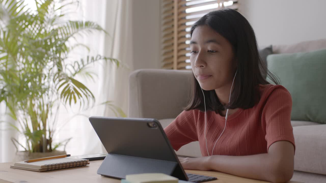 一个亚洲女孩通过一个带耳机的平板电脑与导师在线学习视频素材