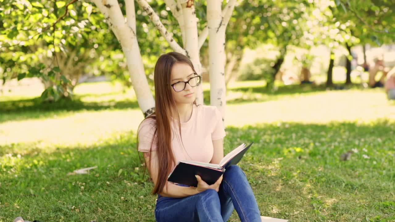 快乐的少年在大学前公园的草地上学习，一个学生看书，学习科目视频素材