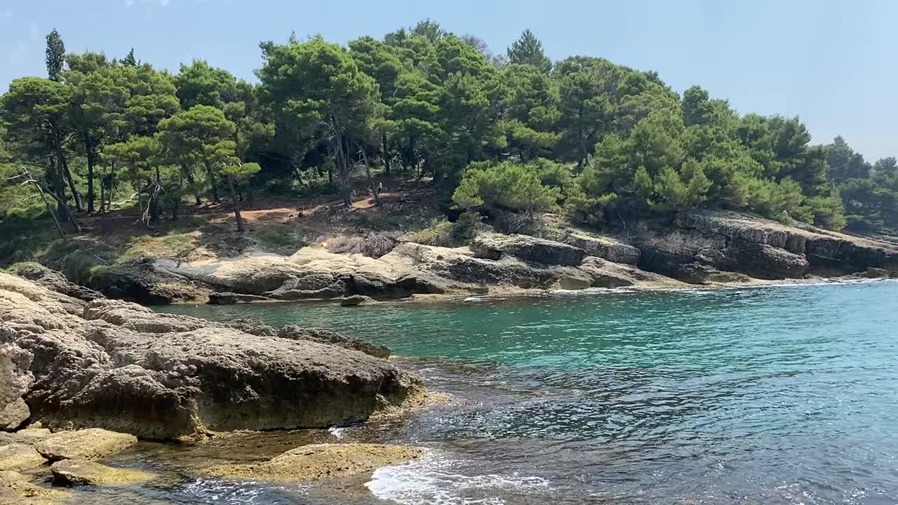 阳光明媚的夏日，美丽的海岩海岸环绕着松林。蓝绿色的地中海海水。田园诗般的自然景观。海岸上的针叶树。视频素材