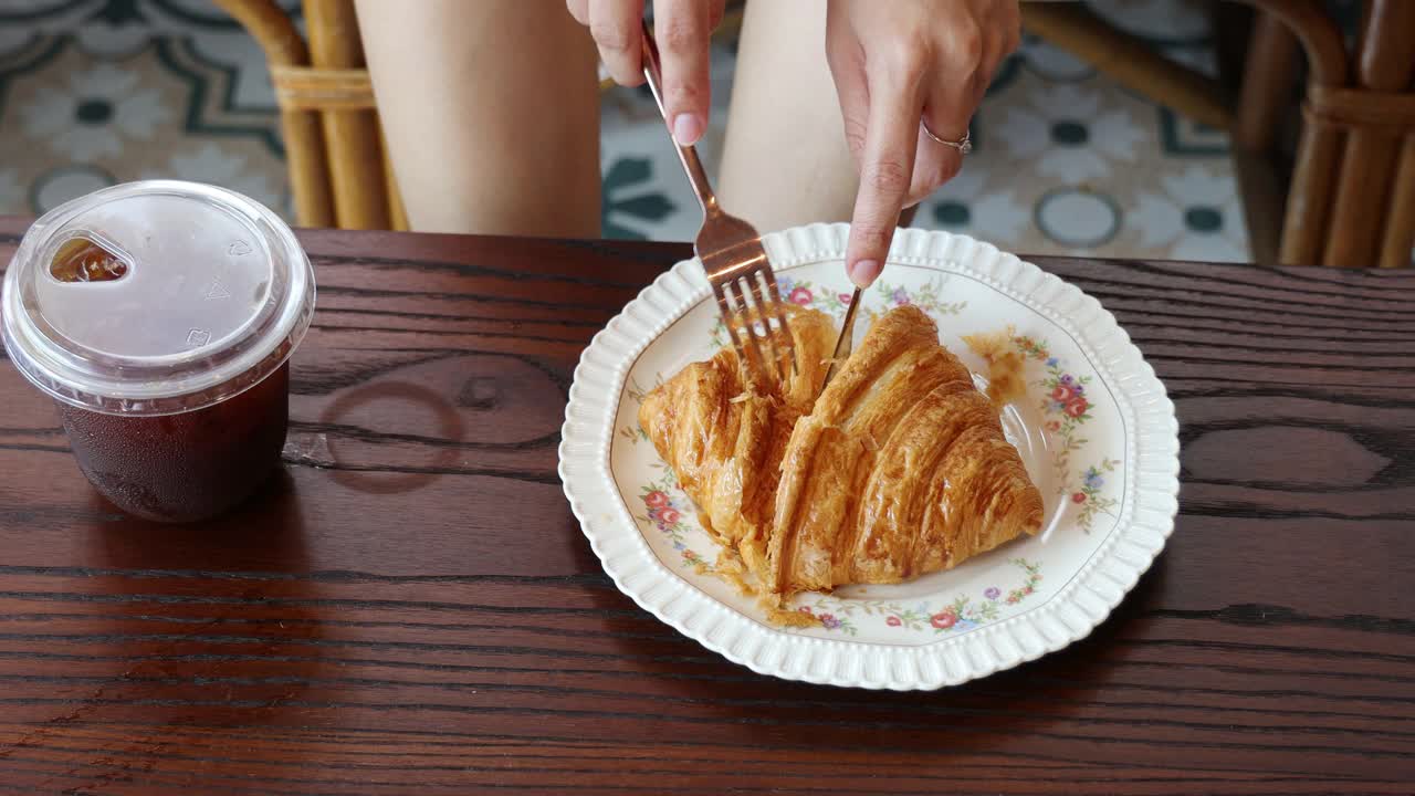 年轻女子在吃美味的羊角面包，并咬它。迷人的女士早上在家享受甜食。饮食、美容、生活方式视频素材