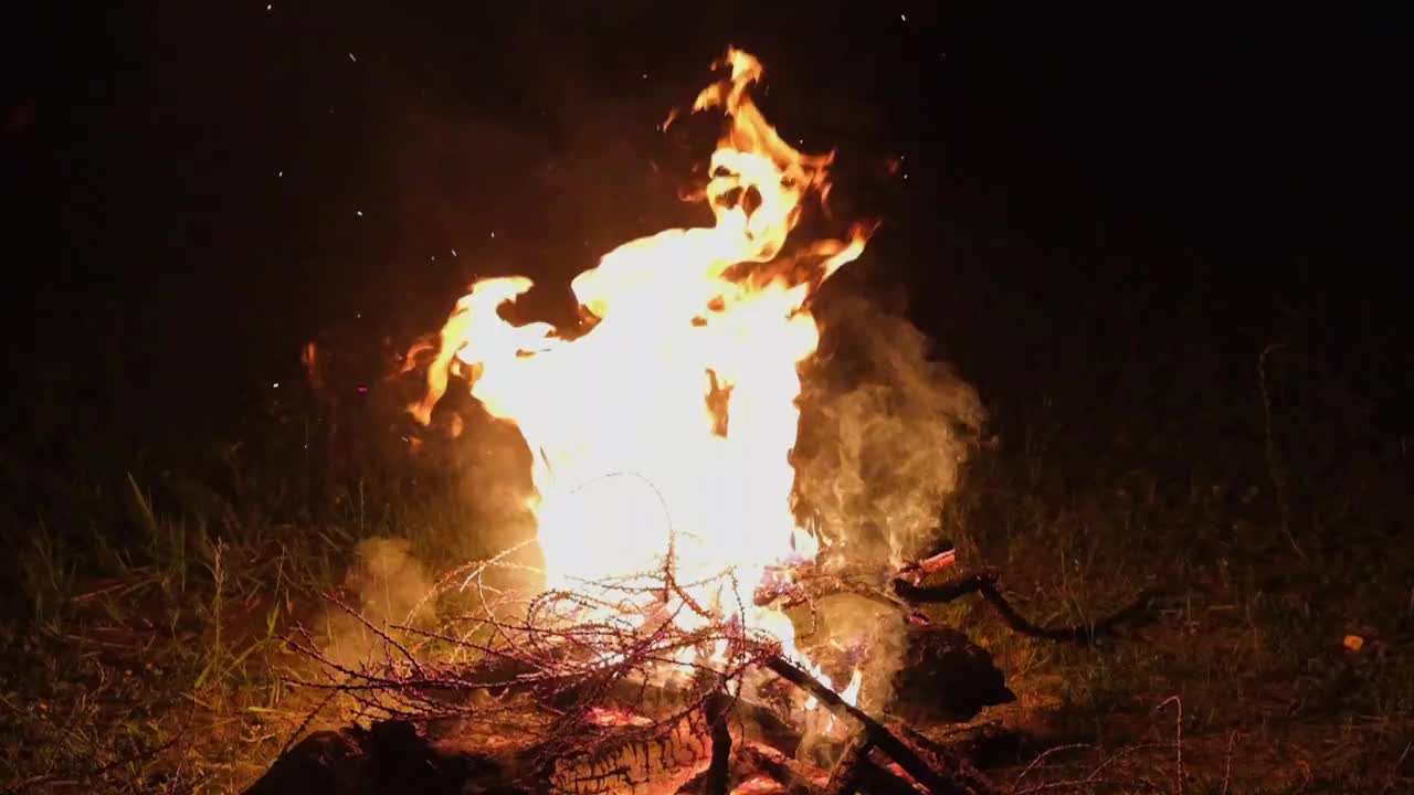 晚上篝火。柴火燃烧着，火焰很大，火星飞溅，烟雾缭绕，动作缓慢。视频素材