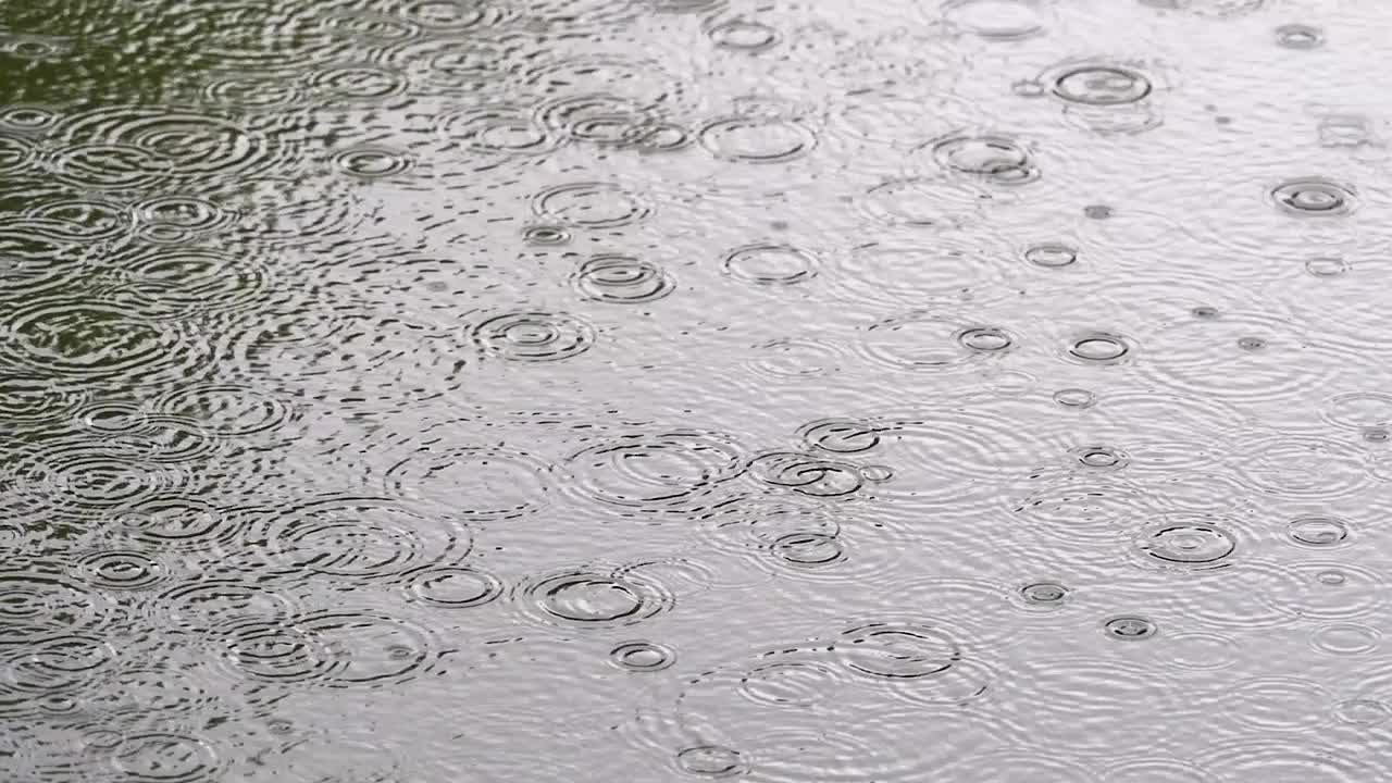 侧视图雨点落入池塘的慢动作，水面涟漪。视频素材