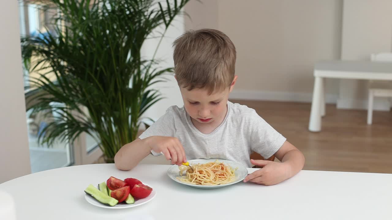 一个小男孩在厨房里微笑着在家吃意大利面。好孩子食欲概念视频素材