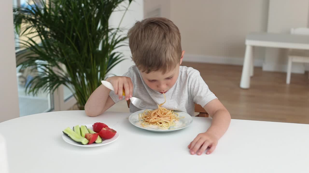 一个小男孩在厨房里微笑着在家吃意大利面。好孩子食欲概念视频素材