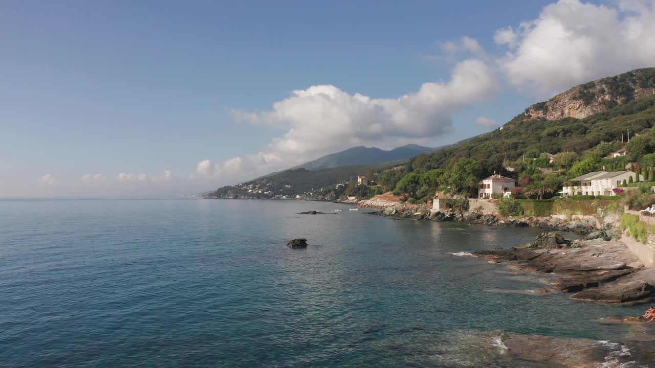 夏日阳光明媚的科西嘉岛海岸线上的特色房屋鸟瞰图。岩石海岸，生动的蓝色海洋，绿色植被上的山丘，树木，山脉的背景视频素材