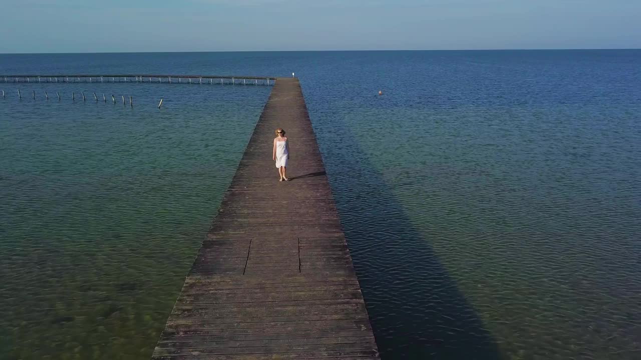 一个女人走在海边的一个木制码头上视频素材