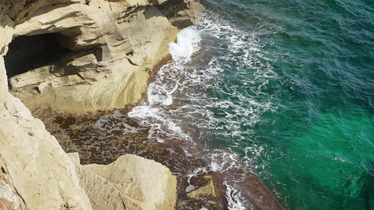 在一个阳光明媚的日子里，小海浪拍打着岩石海岸，从上面看，慢动作视频视频素材