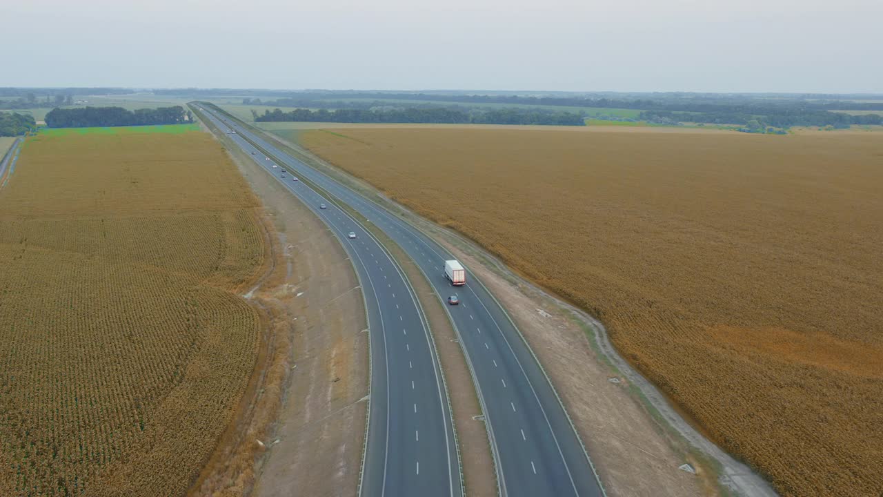 一辆带着拖车的白色卡车沿着高速公路在田野间行驶，空中拍摄着小麦的照片视频素材