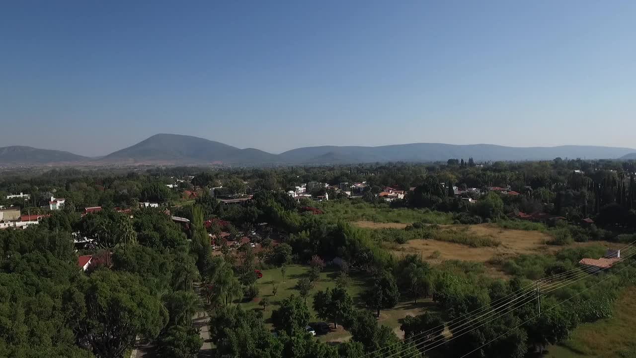 无人机上升，飞过森林，飞向背景为小山的停车场视频素材